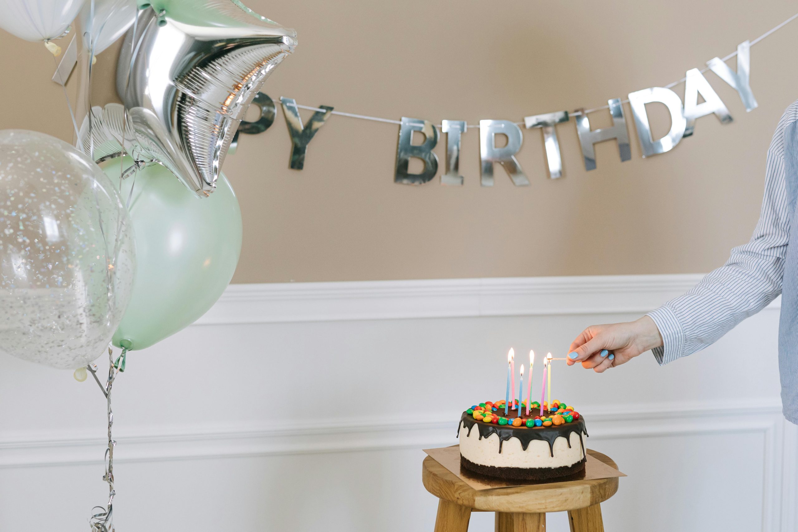 Bright birthday setup featuring a cake with candles, balloons, and a happy birthday banner.